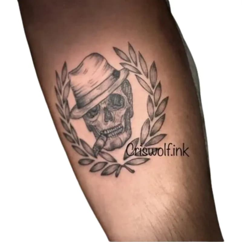 Tatouage crâne au chapeau entouré d'une couronne de laurier sur bras, Le Papillon Qui Pique Montbéliard